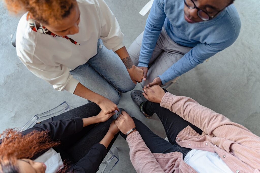 Four people sit in a circle holding hands, emphasizing unity and support in a therapy session.